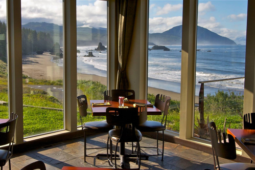 A cozy restaurant with tables overlooking a scenic beach and ocean view, framed by large windows.