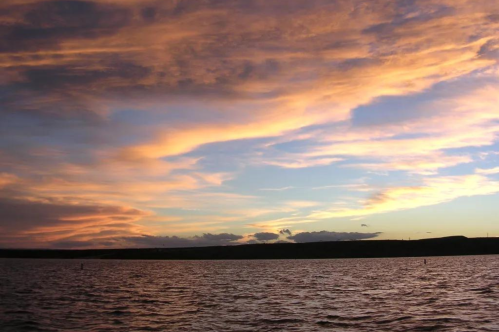 A serene sunset over a calm lake, with vibrant orange and purple clouds reflecting in the water.