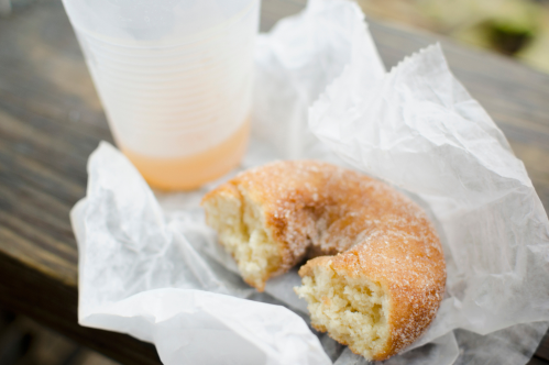 A partially eaten donut on crumpled paper next to a cup of drink on a wooden surface.