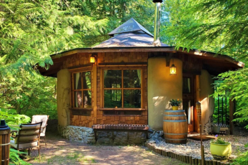 A cozy, round cabin surrounded by lush greenery, featuring wooden accents and a stone foundation.