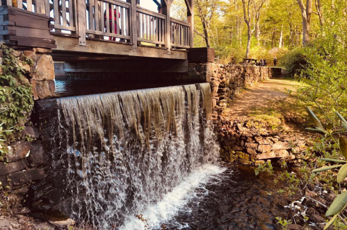 Enchanta bridge surrounded by trees with waterfall flowing beneath at Moore State Park in Paxton, Massachusetts