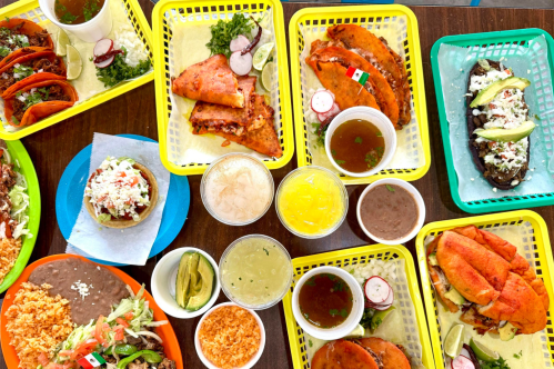 A vibrant spread of Mexican dishes including tacos, enchiladas, and drinks, served in colorful baskets.