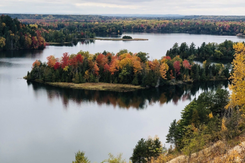 A serene lake surrounded by vibrant autumn foliage and a small island, reflecting colorful trees in the water.