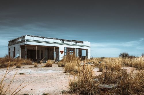 Abandoned building surrounded by tall grass under a cloudy sky, showcasing a desolate and eerie landscape.