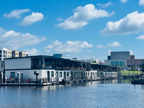 Modern floating buildings along a calm waterway, with a blue sky and fluffy clouds in the background.