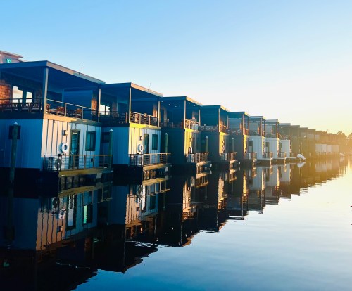 Row of modern houseboats reflecting in calm water at sunrise.