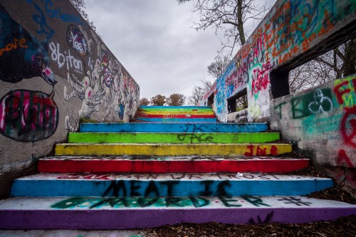 Colorful graffiti-covered stairs lead upward under a cloudy sky, with vibrant hues of pink, green, and blue.