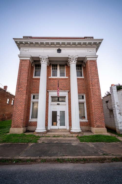 Historic brick building with tall white columns, an American flag, and large windows, set against a clear sky.