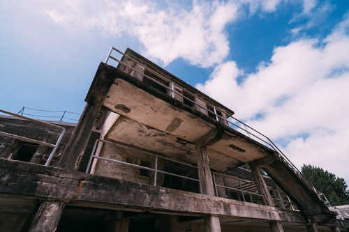 Abandoned building with a weathered facade, featuring a balcony and a blue sky with scattered clouds above.