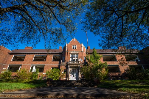 An old brick building with a decorative entrance, surrounded by trees and a clear blue sky.
