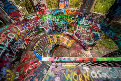 A spiral staircase covered in colorful graffiti, surrounded by greenery.