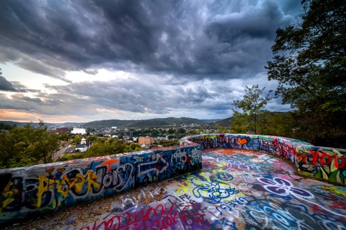 A colorful, graffiti-covered overlook with a dramatic sky and distant hills in the background.