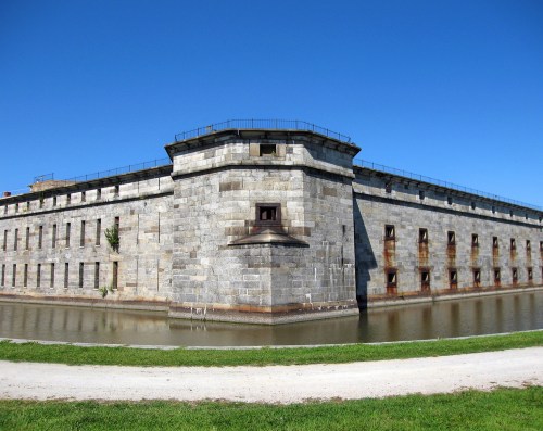 Historic stone fortress with a moat, featuring a clear blue sky and green grass in the foreground.