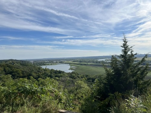 A scenic view of a river winding through lush greenery under a blue sky with wispy clouds.