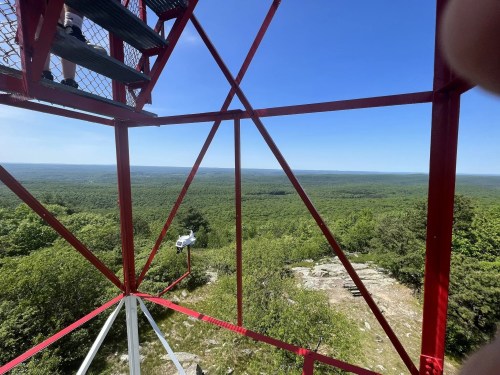 View from a red observation tower overlooking a lush green landscape and distant hills under a clear blue sky.