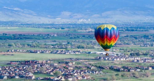 A hot air balloon flying over a suburban landscape with the Rocky Mountains in the distance.