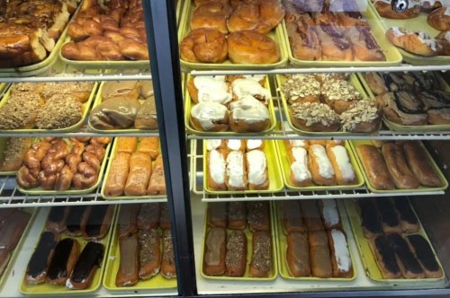 A display case filled with various types of pastries and donuts, arranged on yellow trays.