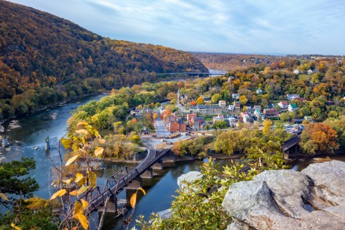 Aerial view of a small town surrounded by autumn foliage, with a river and train tracks in the foreground.