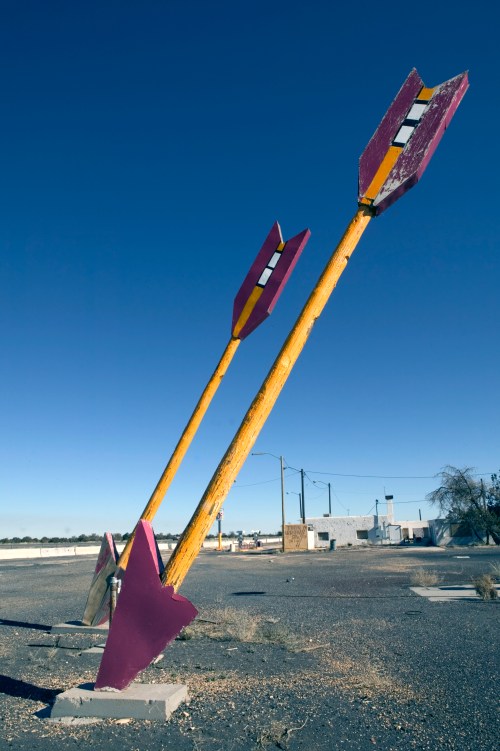 Three large, colorful arrows point upward against a clear blue sky in an abandoned area.