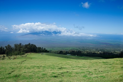 A panoramic view of a lush green landscape with distant mountains and clouds under a bright blue sky.