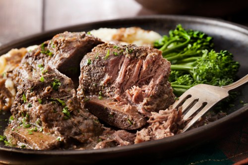 A plate of tender, sliced beef roast with gravy, served alongside mashed potatoes and steamed broccoli.