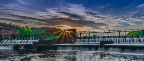 A scenic view of a waterfall at sunset, with vibrant clouds and greenery surrounding a dam structure.