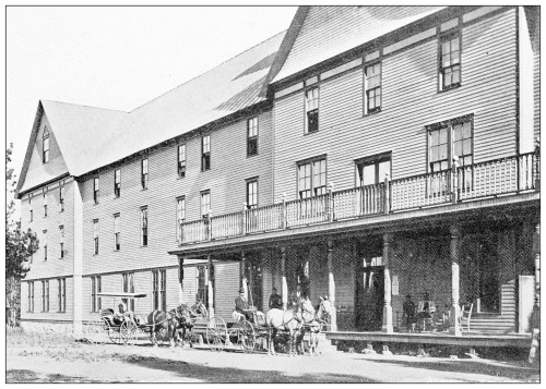 Historic building with a large porch, featuring horse-drawn carriages and people gathered outside.