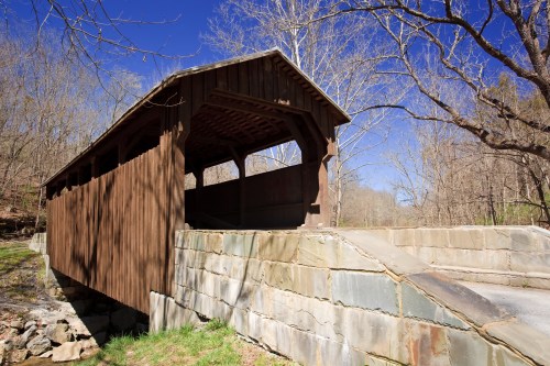 A rustic wooden covered bridge surrounded by bare trees and a clear blue sky.
