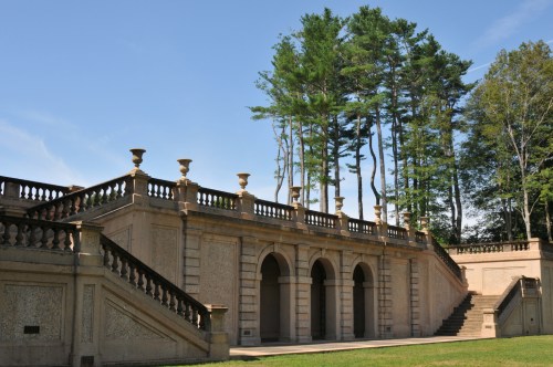 A grand stone staircase with arches, leading to a terrace surrounded by tall trees under a clear blue sky.