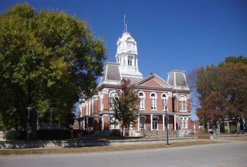 Historic brick courthouse with a clock tower, surrounded by trees and a clear blue sky.