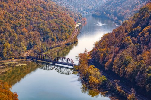 A scenic view of a river winding through autumn-colored hills, featuring a bridge over the water.