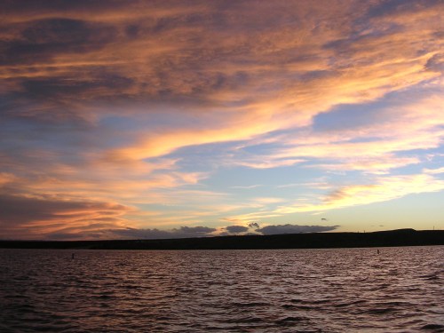 A serene sunset over a calm body of water, with vibrant orange and purple clouds reflecting in the sky.