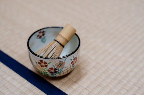 A decorative bowl with a bamboo whisk inside, placed on a tatami mat.