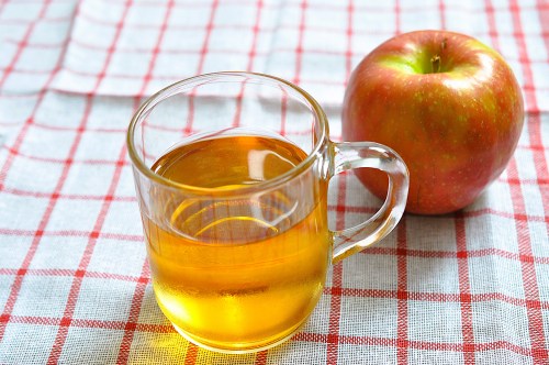 A clear glass cup of golden liquid next to a red apple, set on a checkered tablecloth.