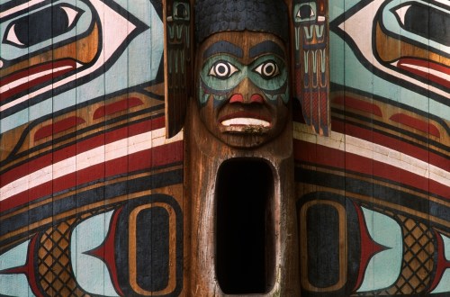 A colorful totem pole featuring intricate carvings of faces and animals, showcasing Indigenous art and culture.
