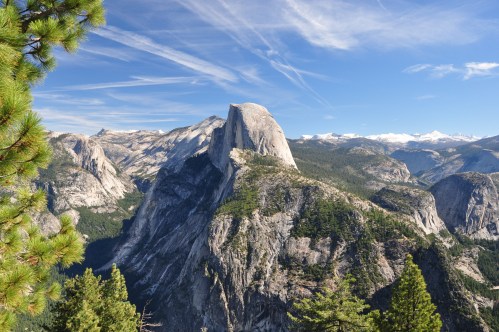 A panoramic view of a mountainous landscape featuring a prominent granite peak under a clear blue sky.