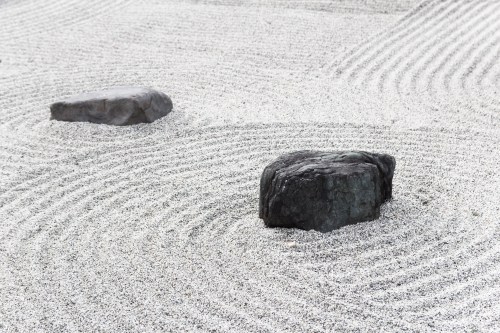 Two rocks sit on a raked gravel surface, creating gentle, swirling patterns around them.