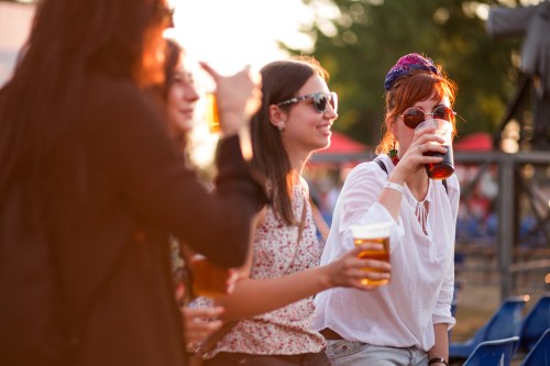 A group of friends enjoying drinks outdoors at a festival during sunset.