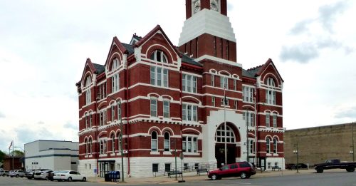 Historic red brick building with white accents and a tall clock tower, set against a cloudy sky.