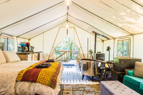 A large bed sits in the middle of a luxurious canvas tent in the woods.