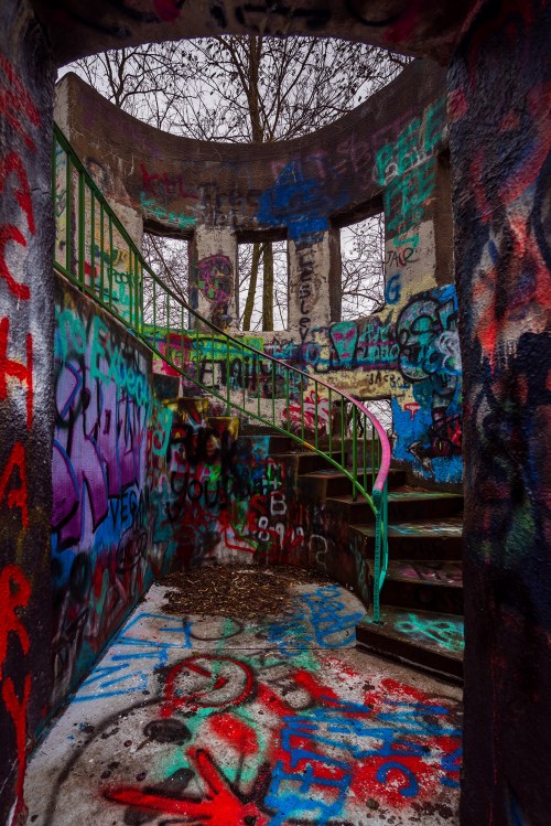 Interior of a graffiti-covered tower with a spiral staircase and colorful walls, surrounded by bare trees.