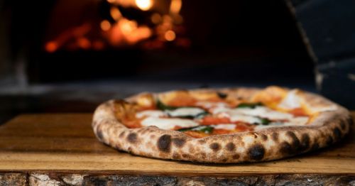 A pizza on a piece of wood outside of an oven.