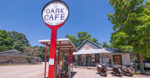 The Oark Cafe and Historic General Store sign stands in front of the rustic building with motorcycles parked outside.