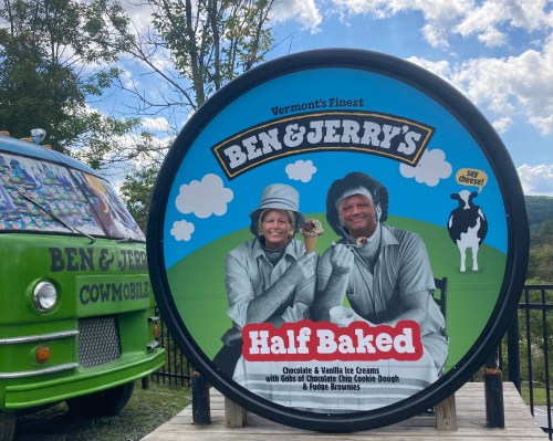A large Ben & Jerry's sign featuring two people in gray outfits holding ice cream, with a scenic background.
