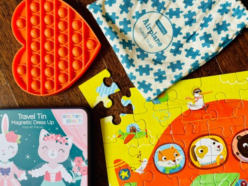 A colorful assortment of children's toys: a heart-shaped popper, a puzzle piece, a dress-up tin, and a vibrant puzzle.