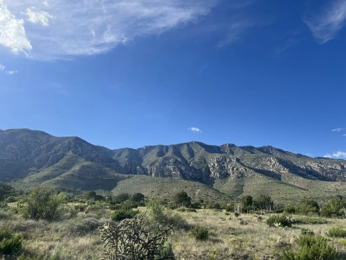 A scenic view of rugged mountains under a clear blue sky, with green vegetation in the foreground.