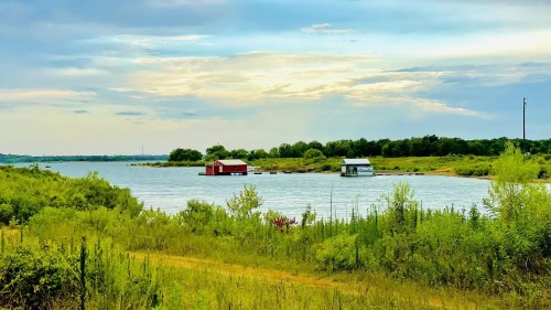 A serene lake scene with two small houses on the water, surrounded by lush greenery and a cloudy sky.