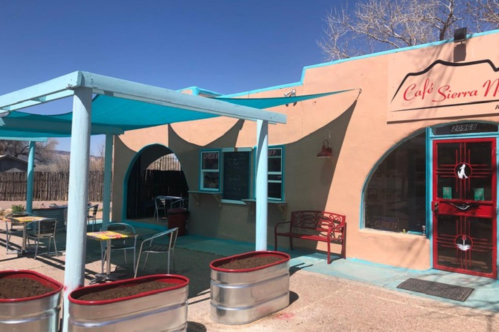 A colorful café with turquoise accents, outdoor seating, and a welcoming "Open" sign on a sunny day.