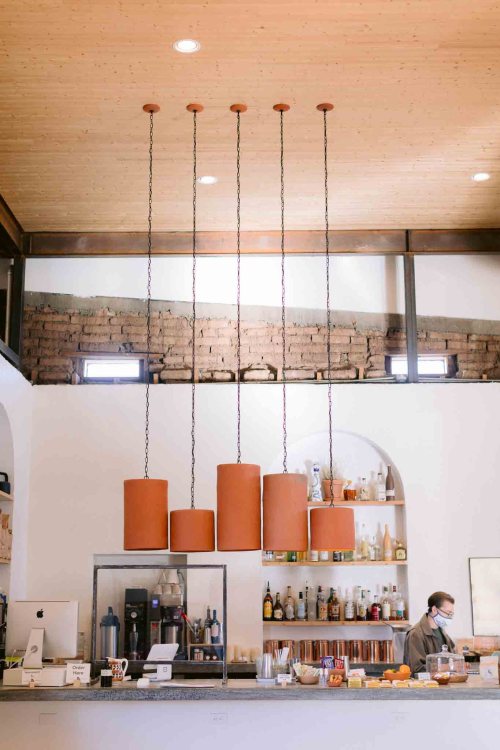 A modern café interior featuring pendant lights, a bar area, and a staff member preparing drinks.