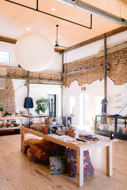 A bright, modern interior of a shop featuring wooden tables, colorful textiles, and decorative items.
